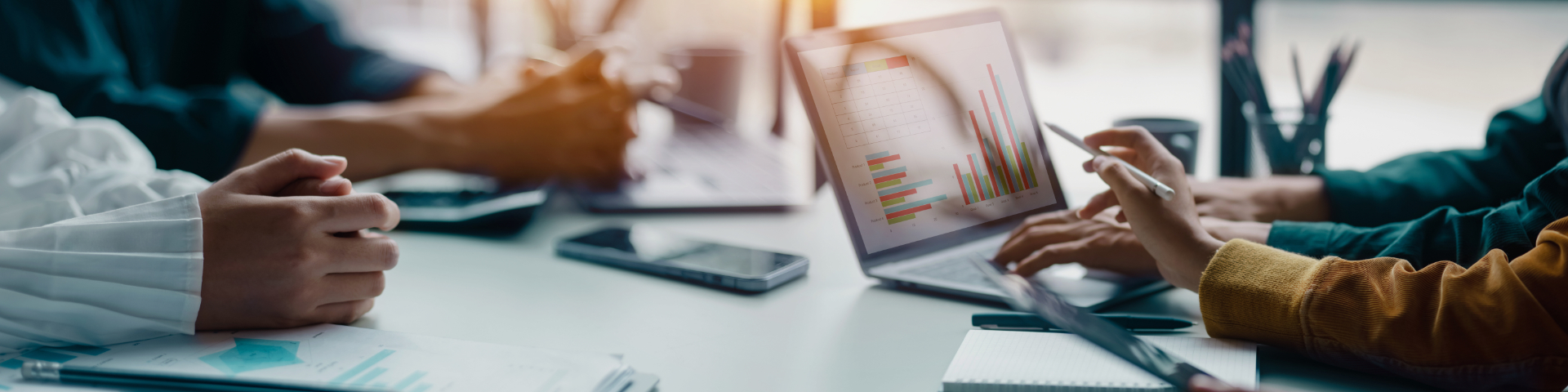 Reunião de negócios com pessoas analisando gráficos e dados em laptops e tablets, discutindo estratégias de crescimento empresarial.