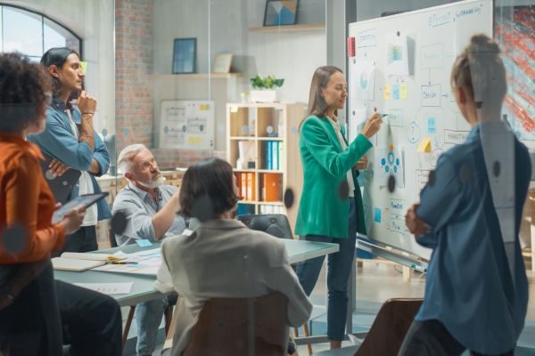 Reunião de equipe em escritório moderno com profissional apresentando ideias em quadro branco, promovendo colaboração e criatividade.