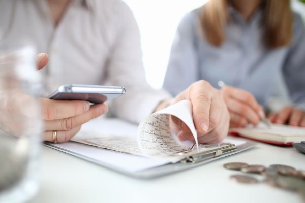 Analisando finanças: um celular e recibo em mãos, com moedas e documentos na mesa. Um momento de planejamento financeiro.