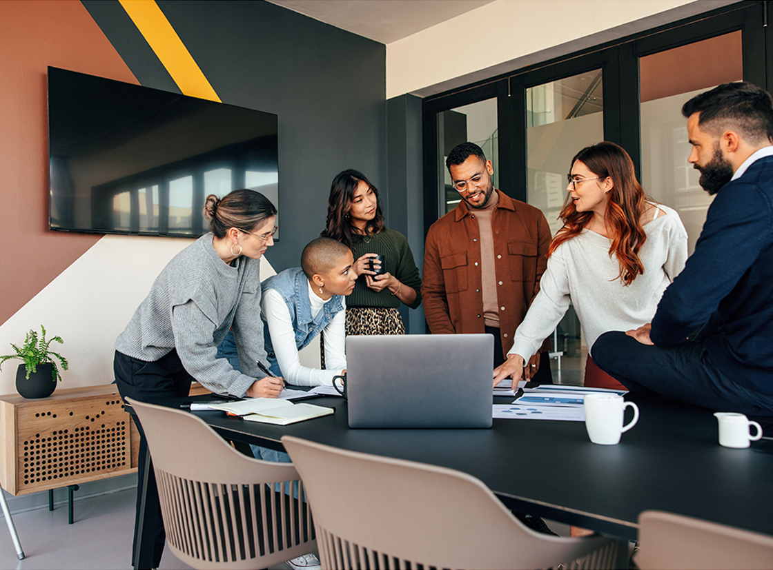 Grupo diverso em reunião ao redor de uma mesa em escritório iluminado, incluindo uma pessoa em cadeira de rodas, destacando inclusão e colaboração