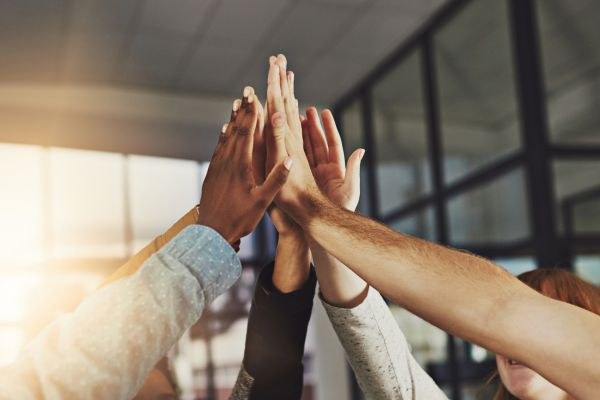 Mãos diversas se unindo em um high five coletivo, simbolizando trabalho em equipe, diversidade e união em ambiente corporativo