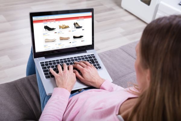 Pessoa navegando em um site de compras online, visualizando uma variedade de sapatos em um laptop. A imagem retrata a experiência de compras pela internet.