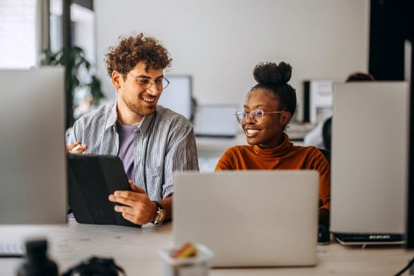 Dois colegas de trabalho colaborando em um projeto, sorrindo e interagindo de forma amigável em um ambiente moderno de escritório