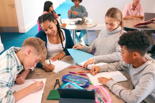 Grupo de estudantes trabalhando em equipe em um ambiente escolar, focando em atividades de aprendizado com material escolar, como cadernos e canetas.