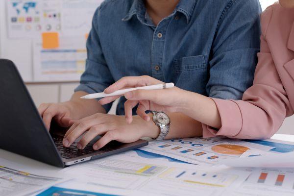 Duas pessoas colaborando em uma análise de dados, utilizando um laptop e gráficos sobre uma mesa, destacando a importância da colaboração em projetos.