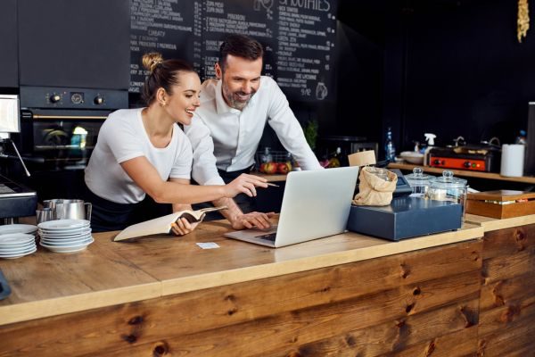 Um homem e uma mulher interagem em um ambiente de café, olhando para um laptop e discutindo ideias sobre negócios.