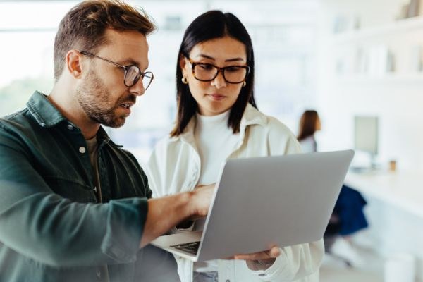 Homem e mulher discutindo sobre um laptop em um ambiente de escritório moderno, demonstrando colaboração e trabalho em equipe.