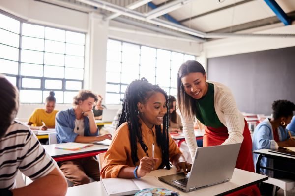 Alunas em sala de aula interagindo com um laptop, destacando o aprendizado colaborativo e a importância da tecnologia no ensino moderno.