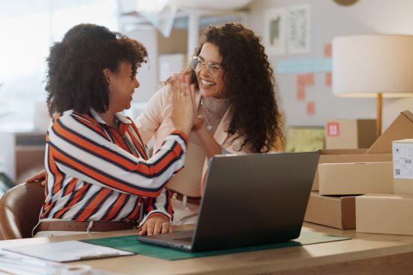 Duas mulheres em um ambiente de trabalho celebrando com um high five, transmitindo cooperação e sucesso em um negócio de vendas online